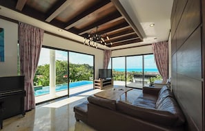 Ein modernes Wohnzimmer mit einem großen Sofa, einem Fernseher und Blick auf einen Swimmingpool und den Ozean.