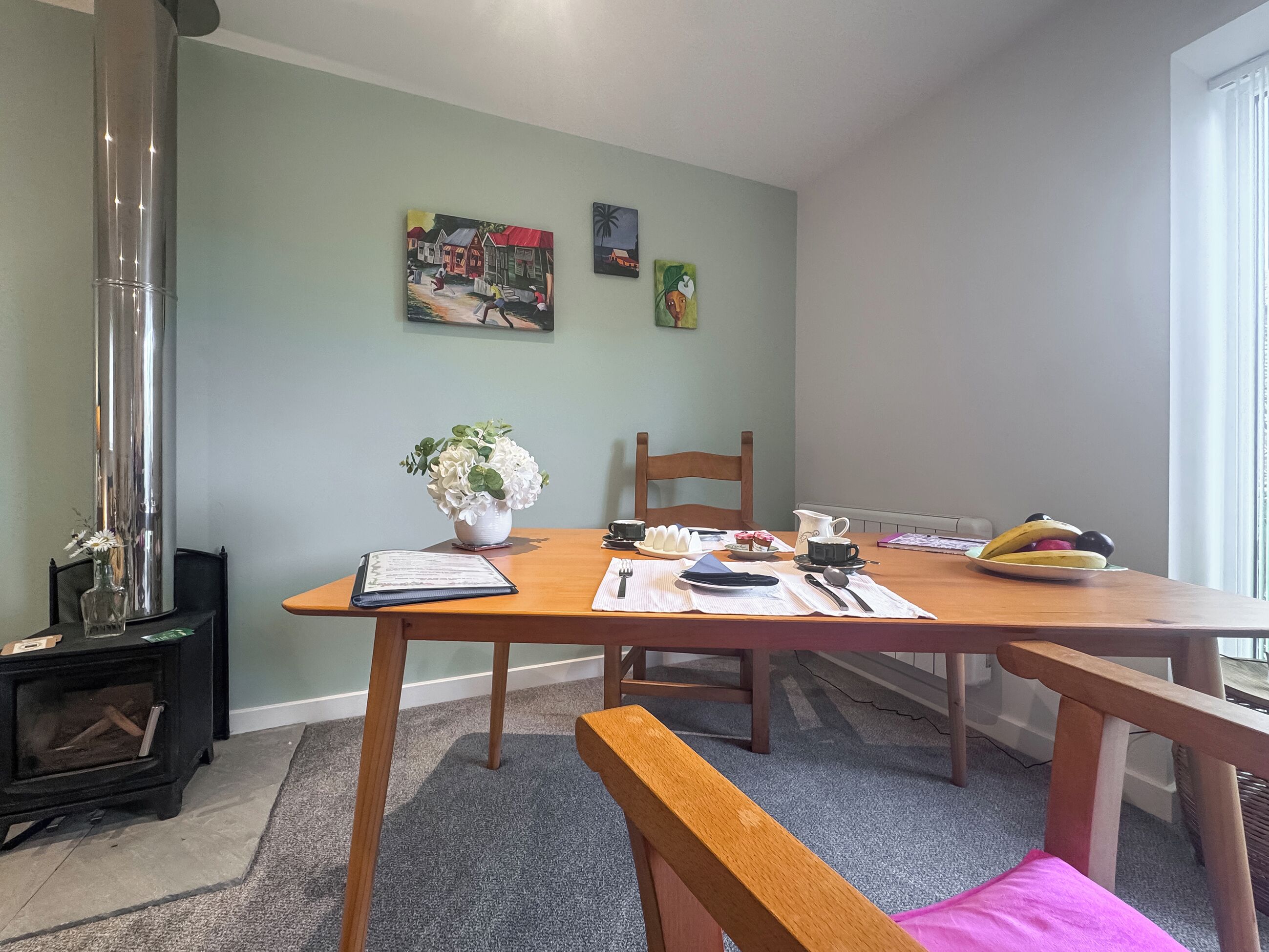 Un coin repas avec une table en bois, des chaises, un vase de fleurs et un tableau accroché au mur.