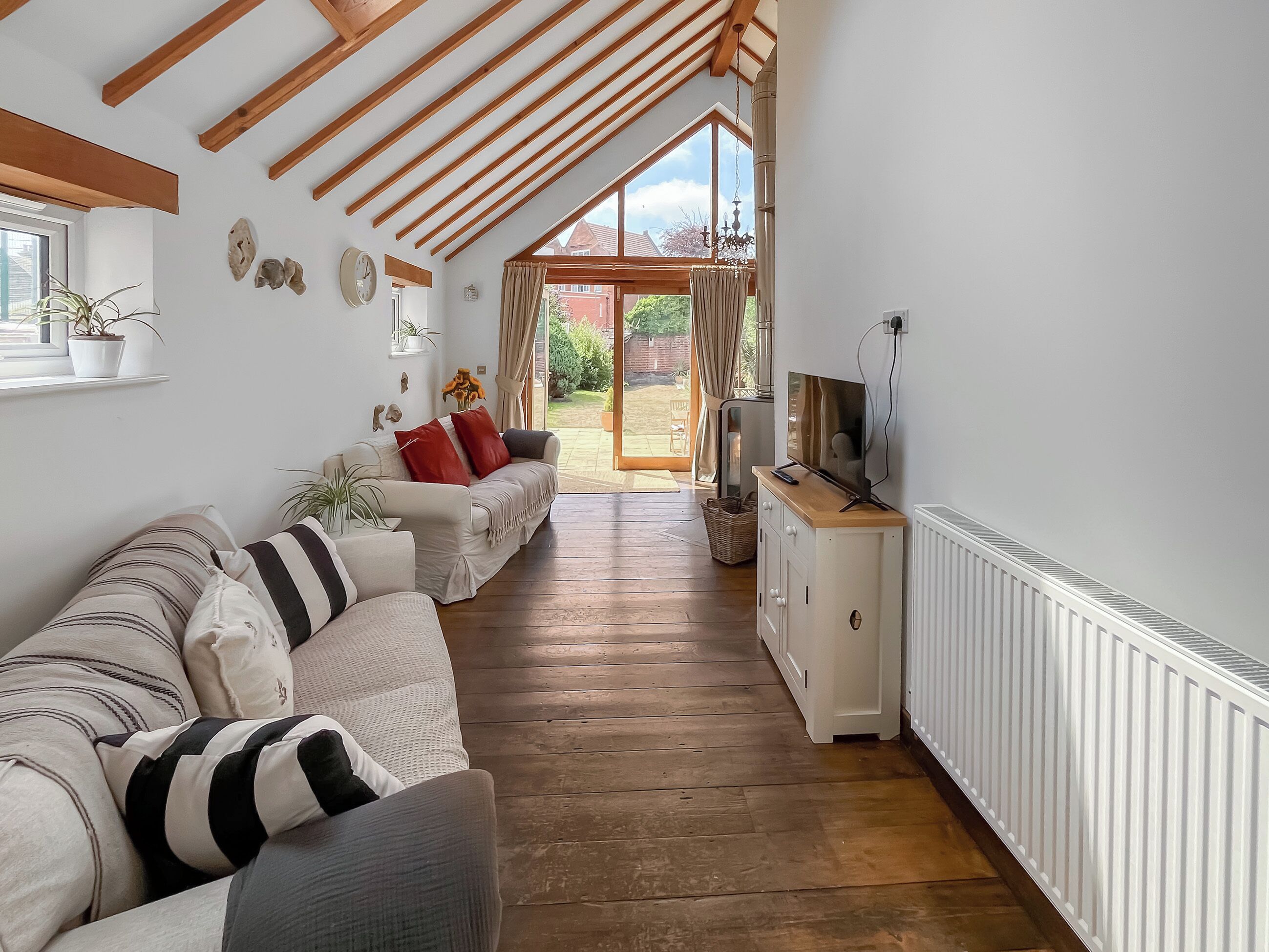 A spacious living room with a wooden ceiling, a sofa set, a television, and a view to the outside.