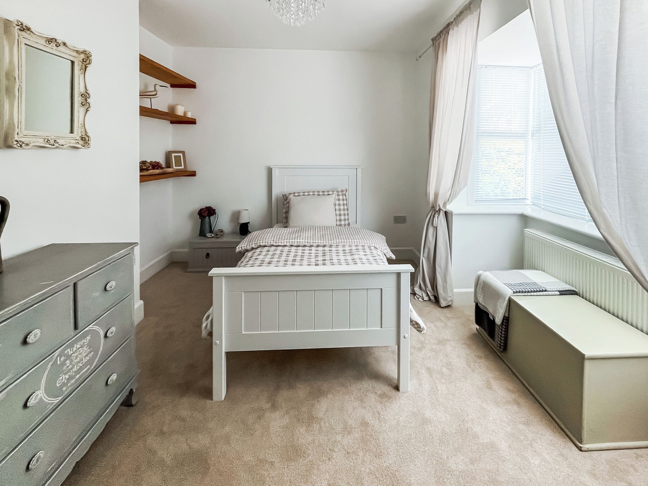 A bedroom with a bed, dresser, bedside table, and a window with curtains.