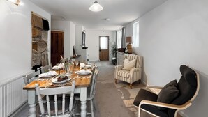 Ein Essbereich mit einem langen Tisch, gedeckt für sechs Personen, umrahmt von weißen Stühlen mit Holzbeinen.