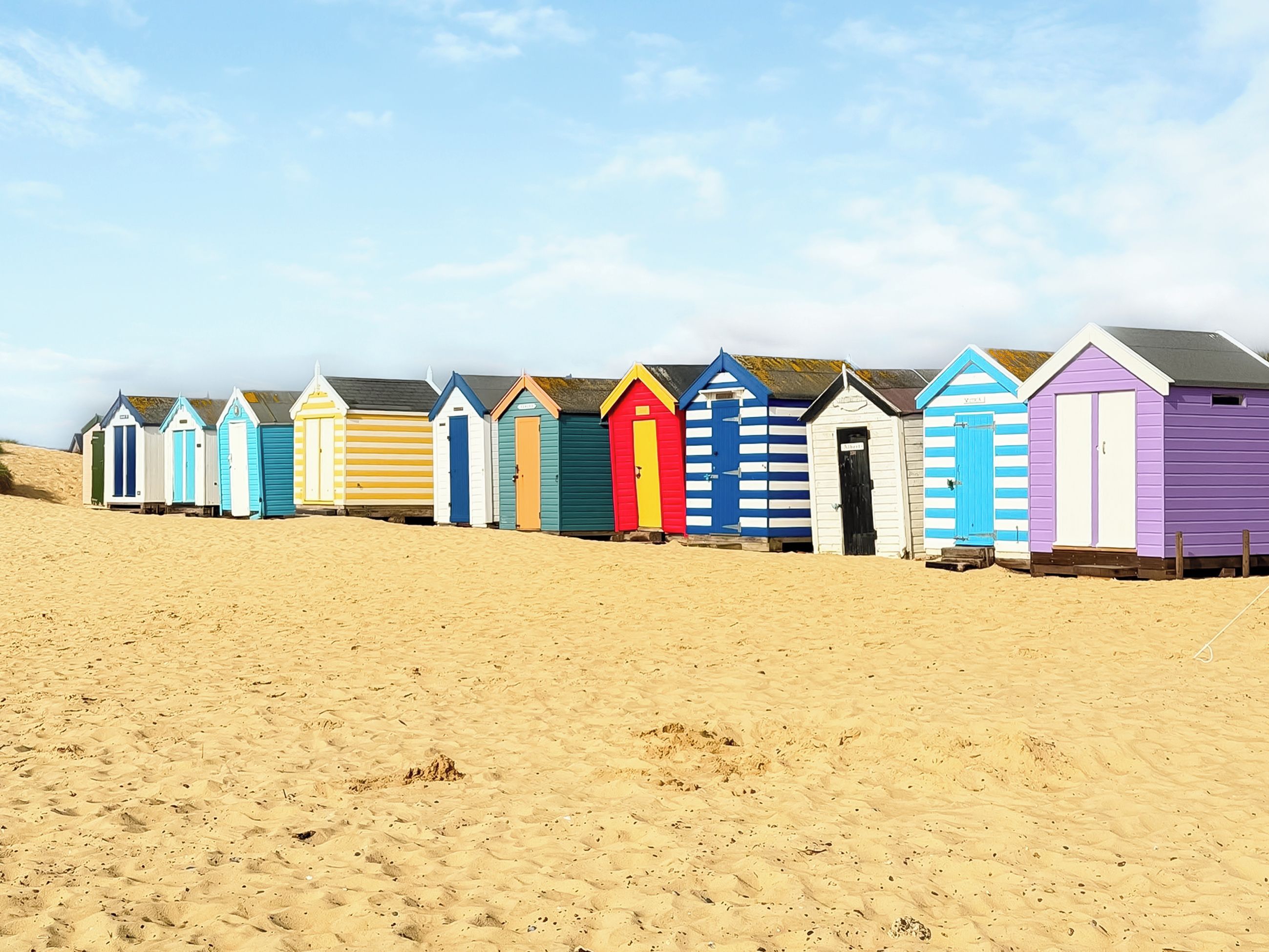A row of beach huts with a sandy beach in the foreground.