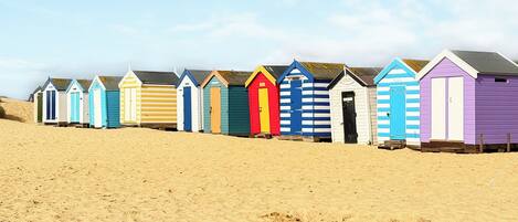 A row of beach huts with a sandy beach in the foreground.