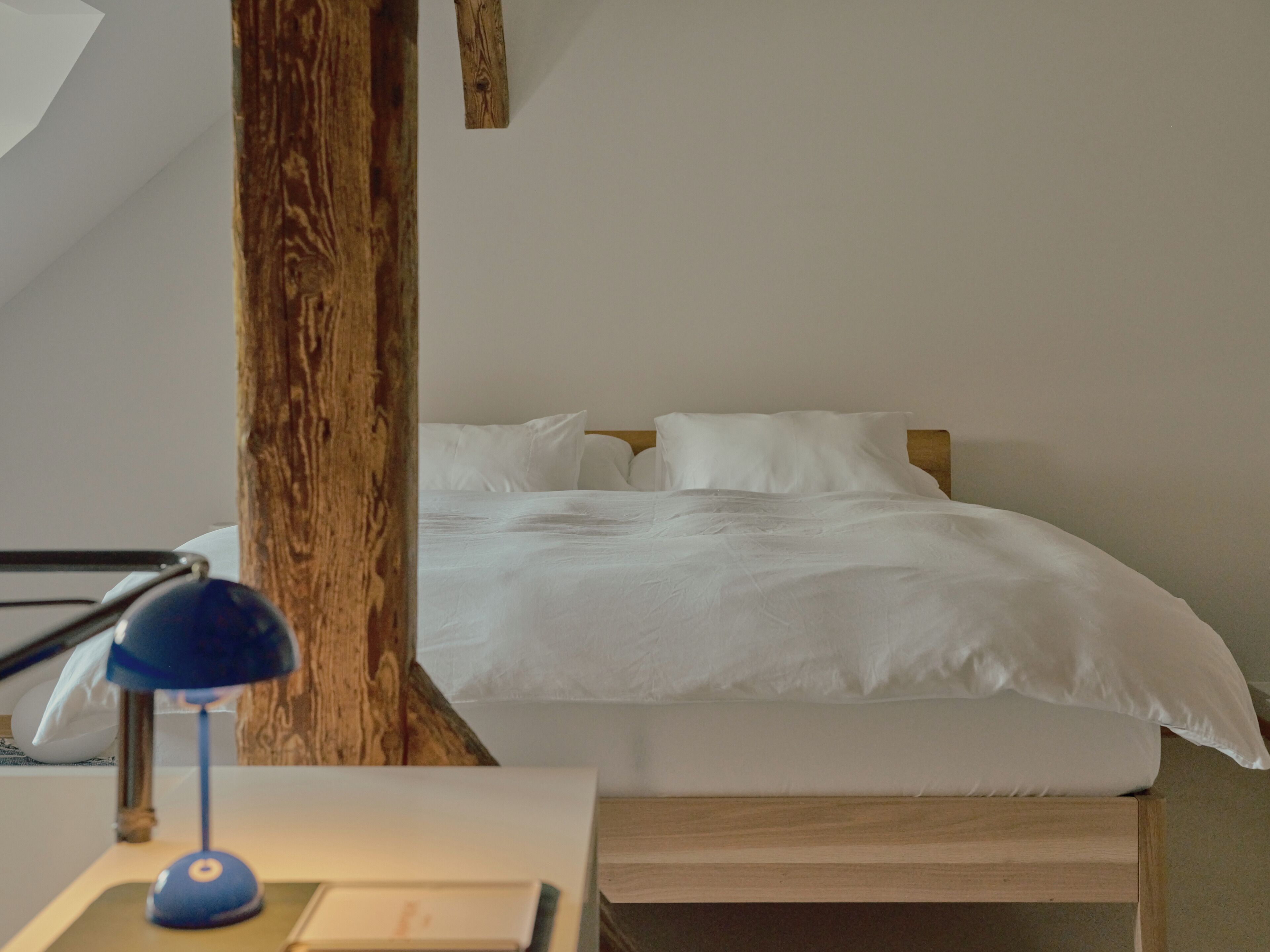 Ein Schlafzimmer mit einem Bett, einem Holz-Kopfteil, einem Schreibtisch mit Lampe und einer weißen Wand.