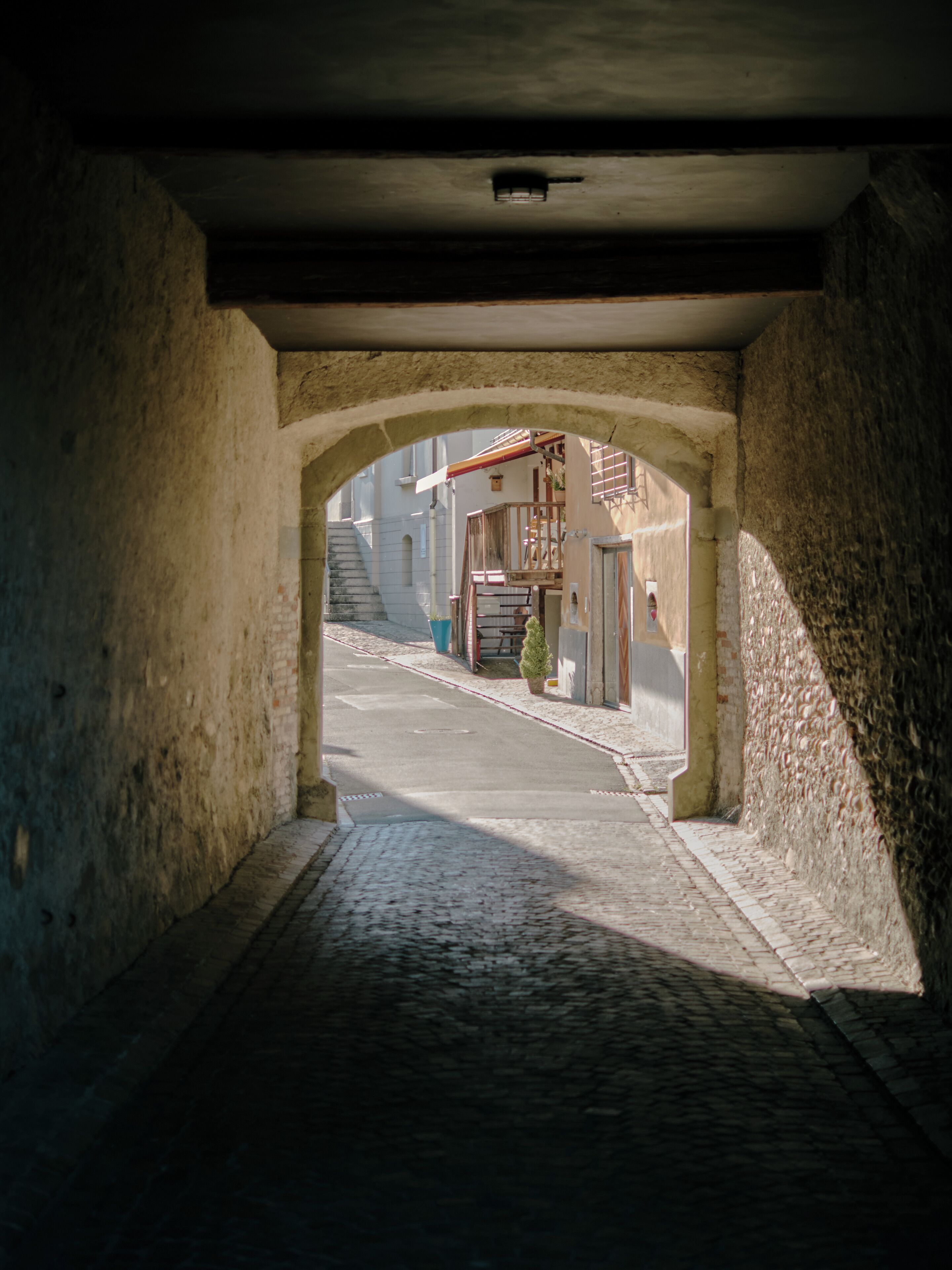 Un passage en arc menant à un bâtiment doté d’un escalier et d’un petit arbre.