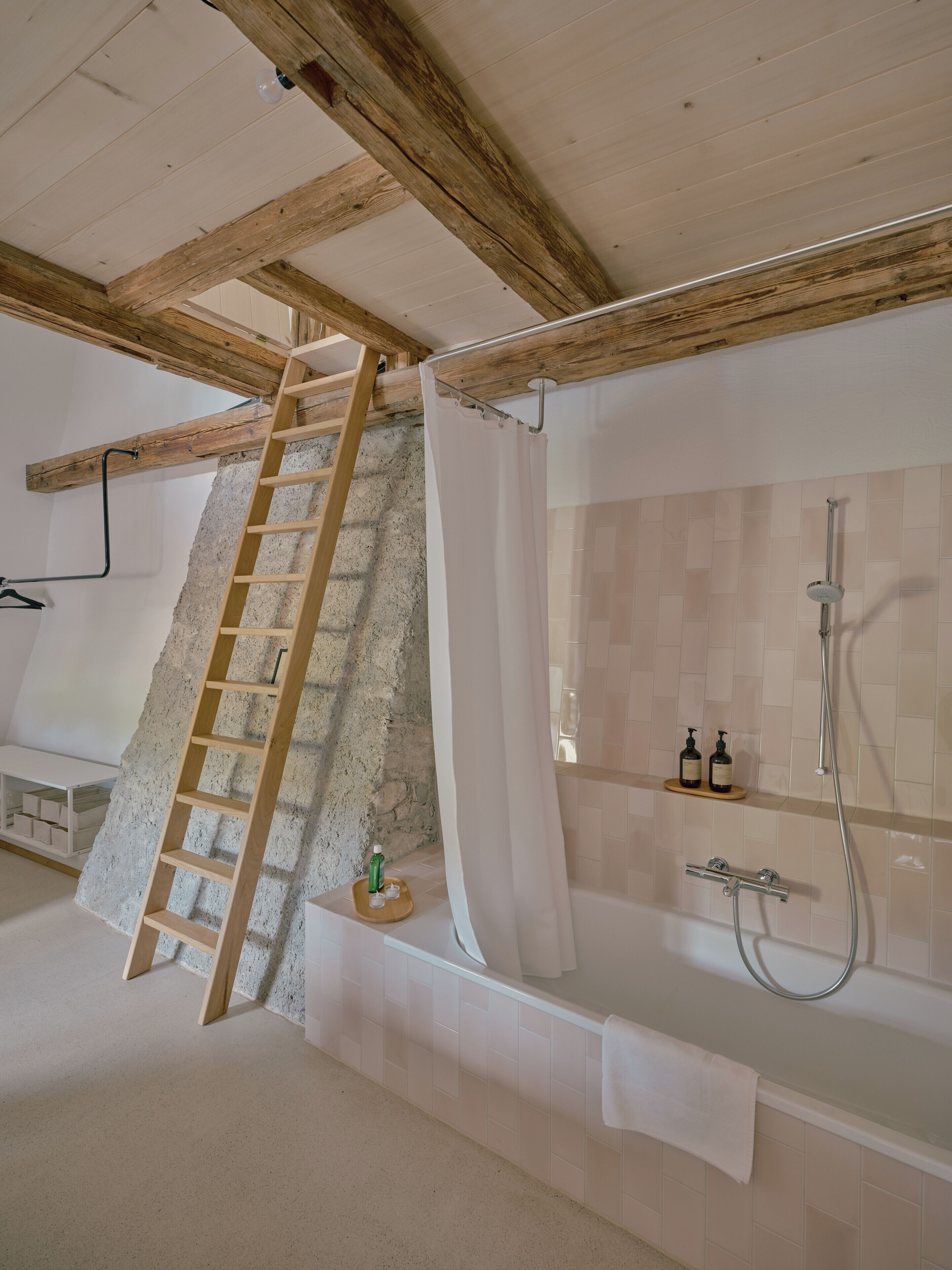 Ein Badezimmer mit Badewanne, Dusche, einer Holzleiter und einer Steinwand.