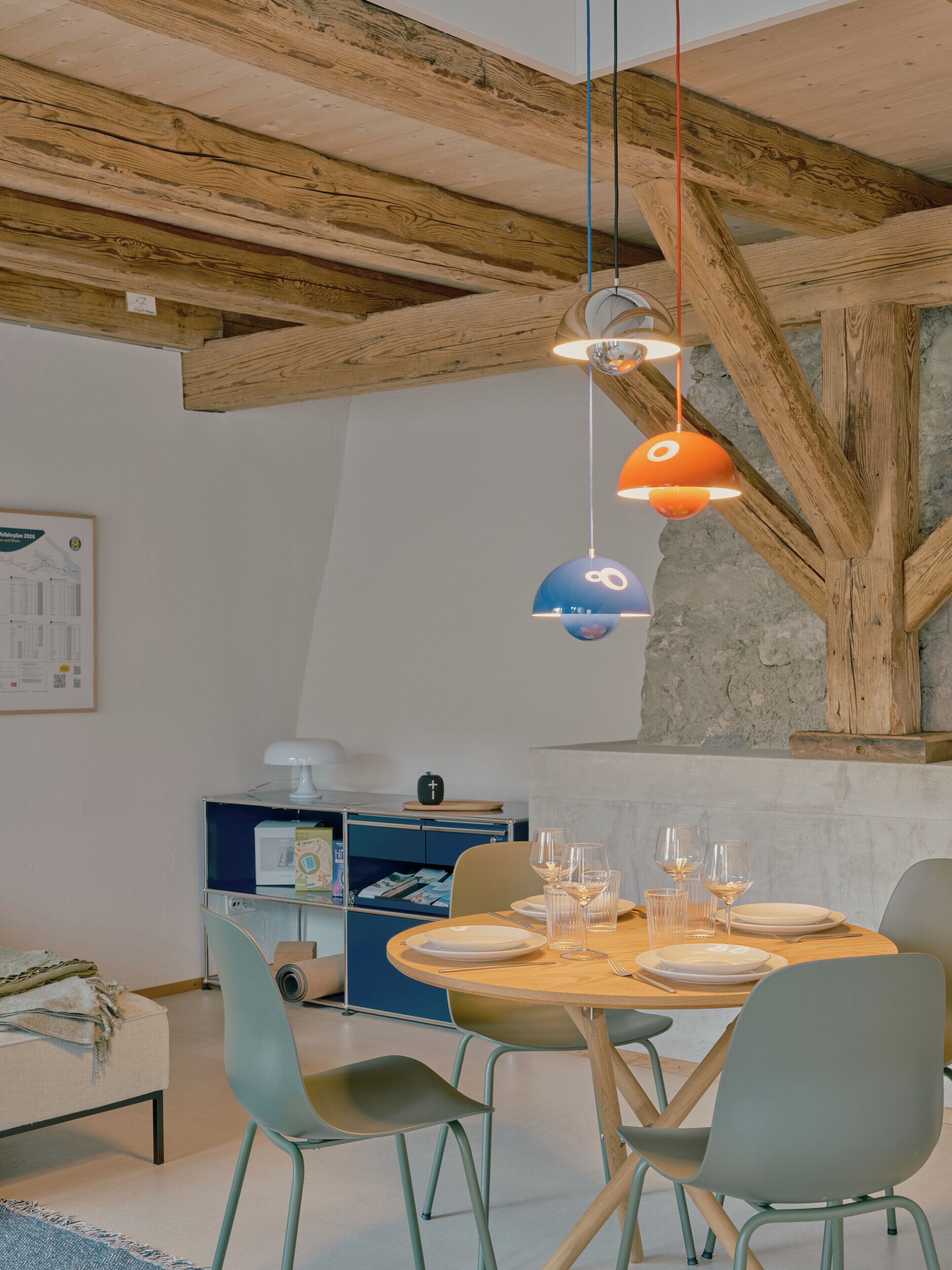 A dining area with a wooden table set for four, surrounded by chairs, under exposed wooden beams.