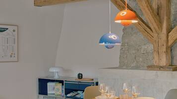 A dining area with a wooden table set for four, surrounded by chairs, under exposed wooden beams.