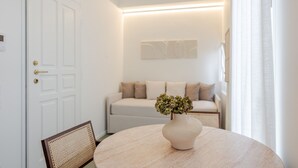 A room with a round table, a white door, a sofa, and a wall-mounted light fixture. - Garibaldi Luxury Suites - Graecalis (Noci)
