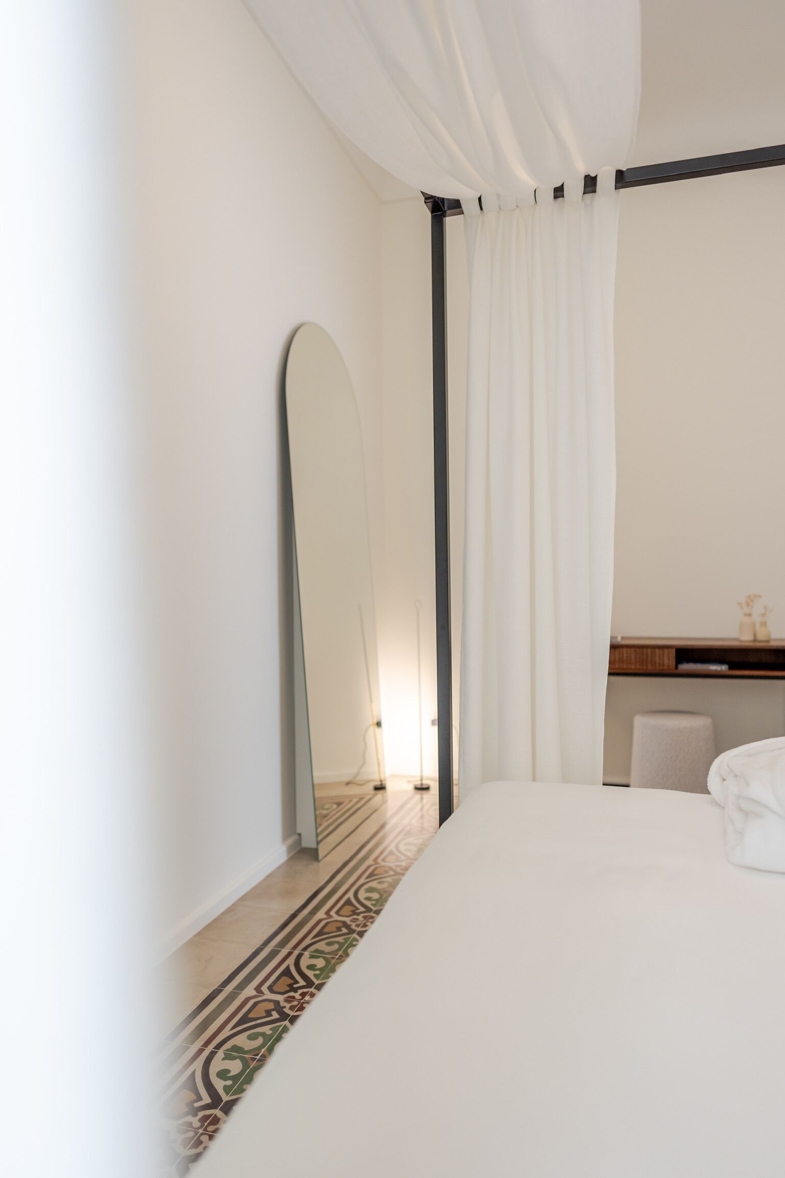 Une chambre avec un grand lit, un miroir, un rideau et un sol à motifs.
