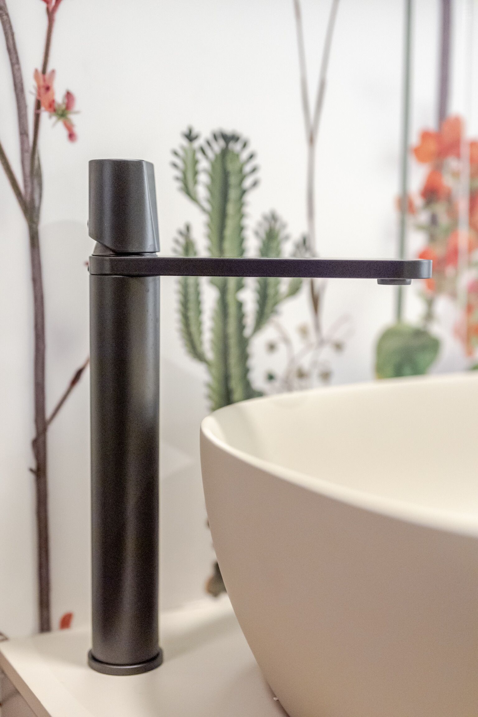 A modern bathroom with a minimalist faucet, a large white basin, and decorative plants in the background.