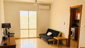 A spacious living area with a sofa, a small table, a ceiling fan, and a laundry area visible through an open door. - Stunning 3-bedroom apartment with a pool – Ideally located in La Zenia! (Orihuela)