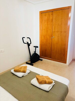 Ein Zimmer mit einem Bett, einem Ergometer und einem Holzschrank.