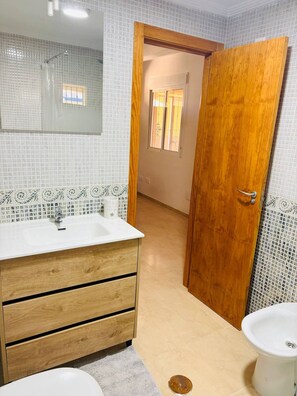 Ein Badezimmer mit einem Holzkosmetikschrank, einem weißen Waschbecken, einem Spiegel und einem Bidet.