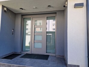 Entrada de un edificio con puertas dobles, un pequeño alero y una cámara de seguridad.