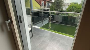Ein Balkon mit Glasgeländer, Blick auf eine grüne Rasenfläche und Häuser im Hintergrund.