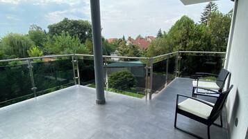 Ein Balkon mit Glasgeländer, einer Metallstütze und einer Sitzecke mit Stuhl und Tisch.