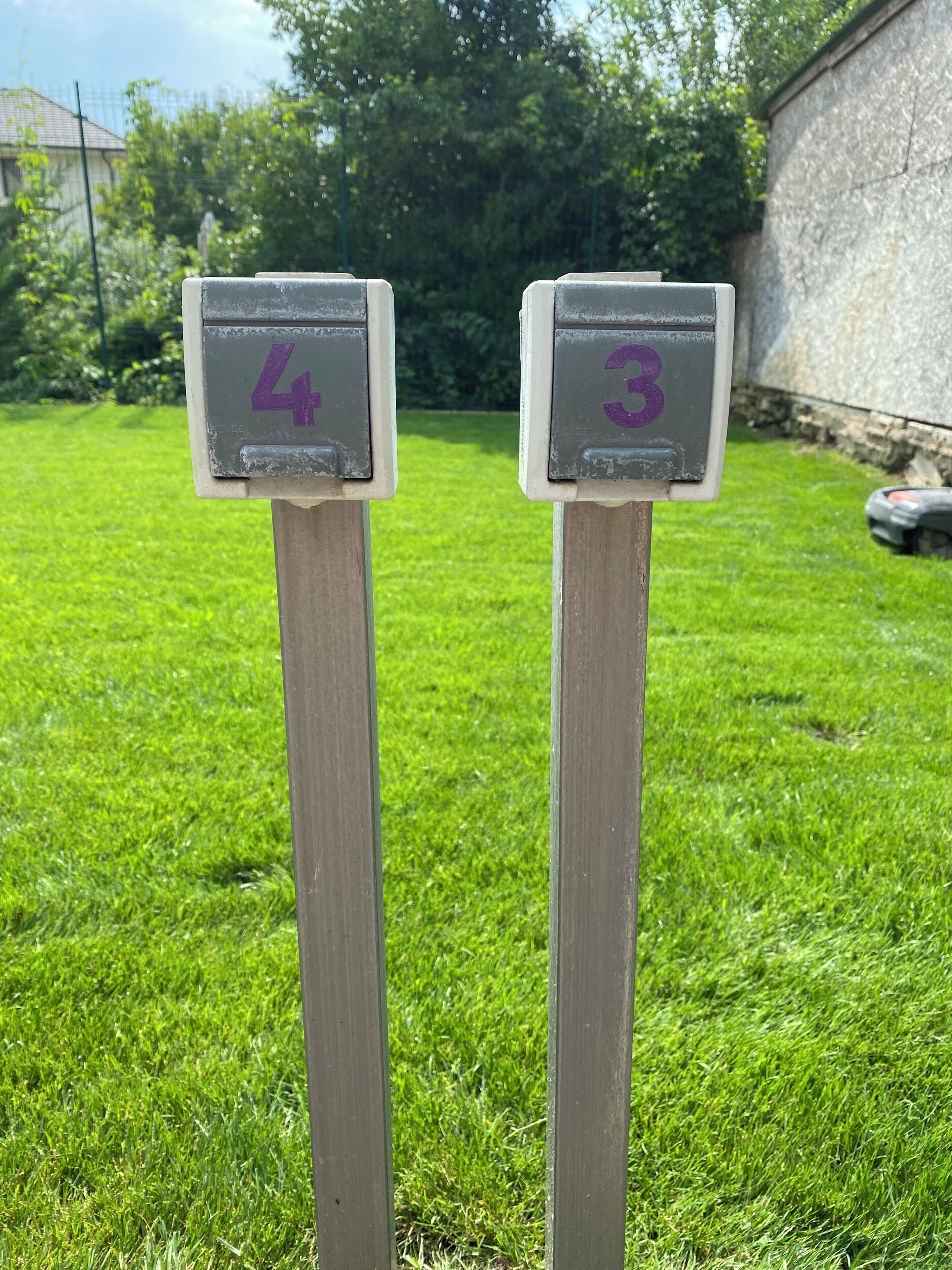 Deux panneaux numérotés, les numéros 4 et 3, fixés à un poteau en bois dans une zone herbeuse.