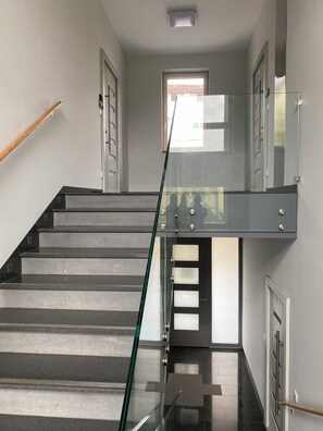 Un interior modern amb una escala, baranes de vidre i una vista a través d'una porta.