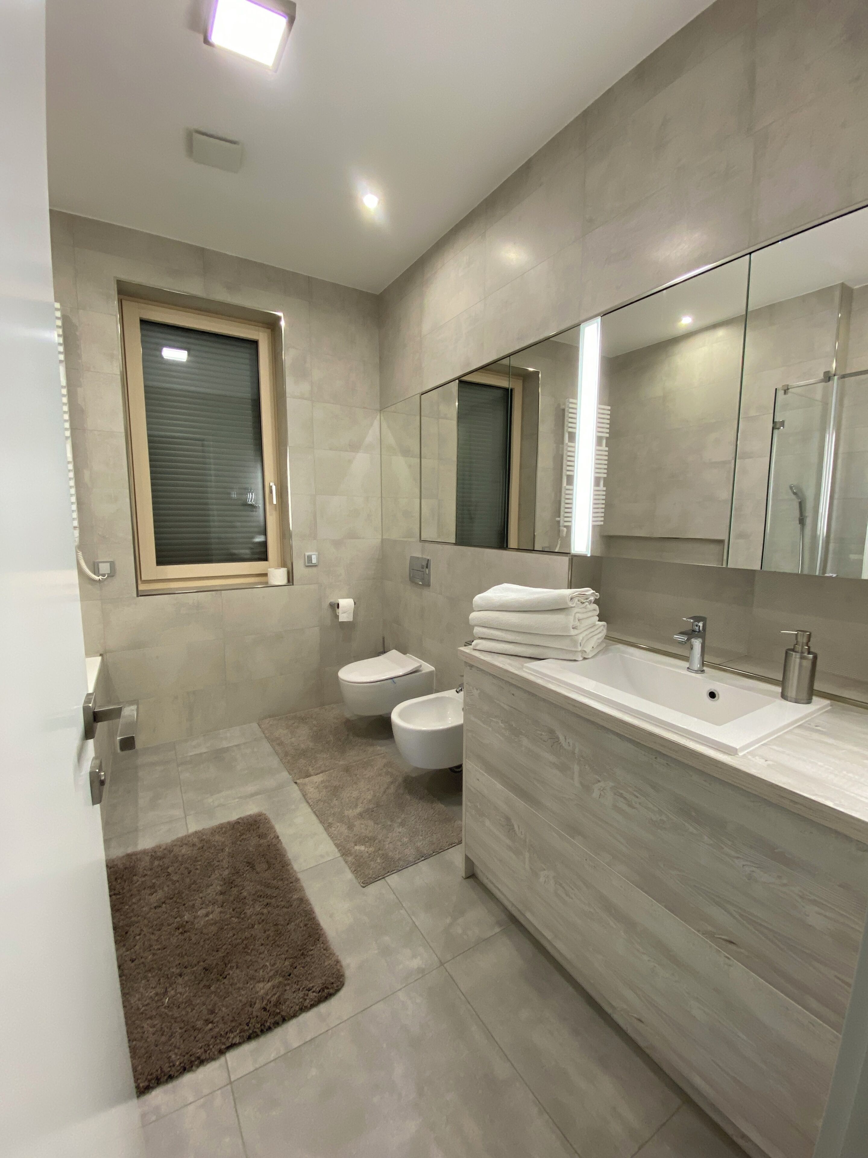 A modern bathroom with a large mirror, a bidet, a toilet, and a bathtub.