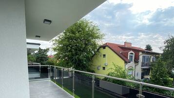 Ein Balkon mit Metallgeländer, gefliestem Boden und Blick auf eine grüne Rasenfläche sowie Gebäude im Hintergrund.