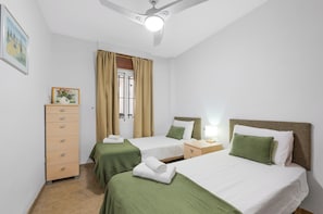 Ein Hotelzimmer mit zwei Betten, einem Schminktisch, einem Nachttisch und einem Deckenventilator.