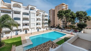 En vy från poolområdet, med ett hotell i bakgrunden, en klarblå pool, vita byggnader och en palm.