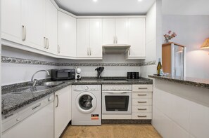 Eine kompakte Küche mit weißen Schränken, einer Waschmaschine, einem Backofen, einer Mikrowelle und einem Spülbecken.