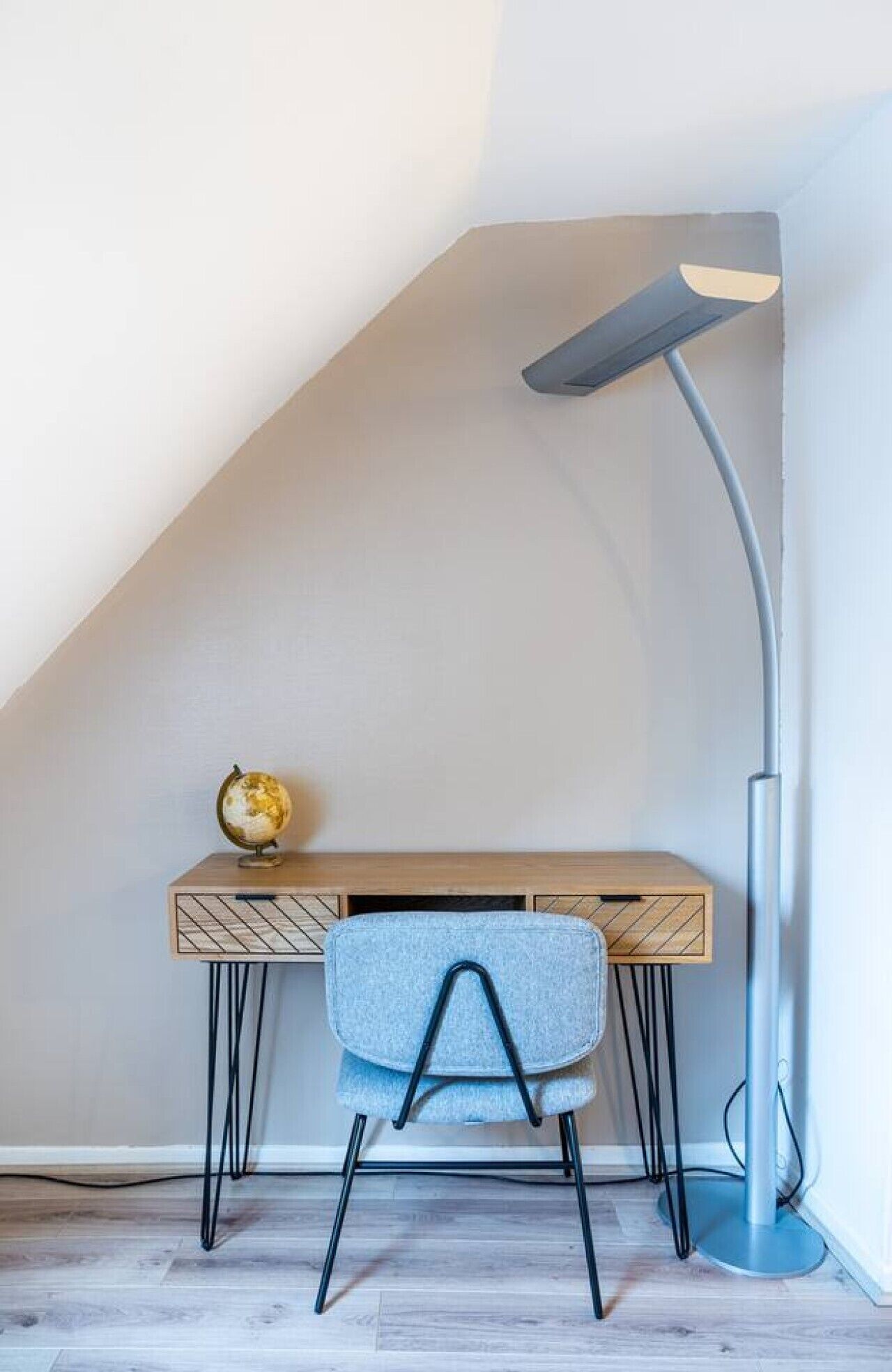 Un bureau avec une chaise, un globe terrestre et une lampe sur pied, dans une pièce dont le plafond est en pente.