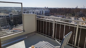 En balkong med utsikt över stadsbilden, ett bord, en stol och ett glas öl.