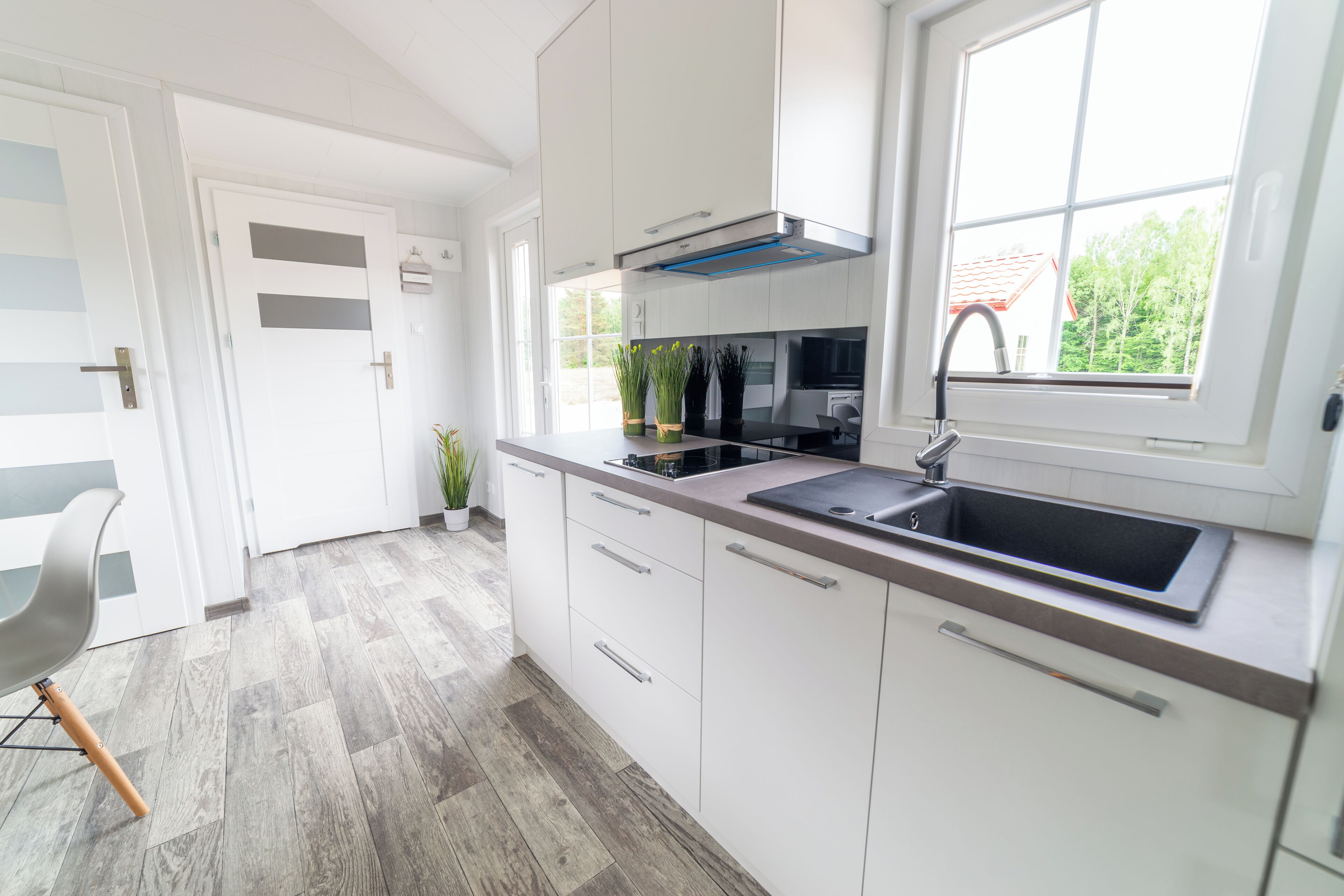 A modern kitchen with white cabinets, a stainless steel sink, and a window with a view of trees.