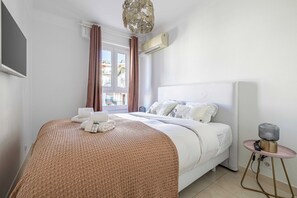 Une chambre d’hôtel comprenant un lit, une table de chevet avec une lampe, une fenêtre avec des rideaux et un appareil de climatisation.