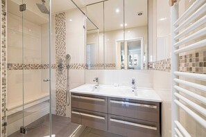 Une salle de bain moderne avec une douche à parois de verre, un meuble-lavabo à deux vasques et un grand miroir.