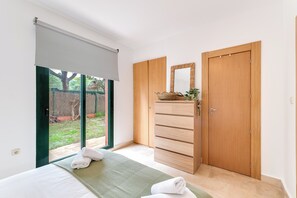 A bedroom with a bed, a wooden wardrobe, a mirror, and a sliding door to a garden. - LXR Marbesa 1-Bedroom Near the Sea (Marbella)