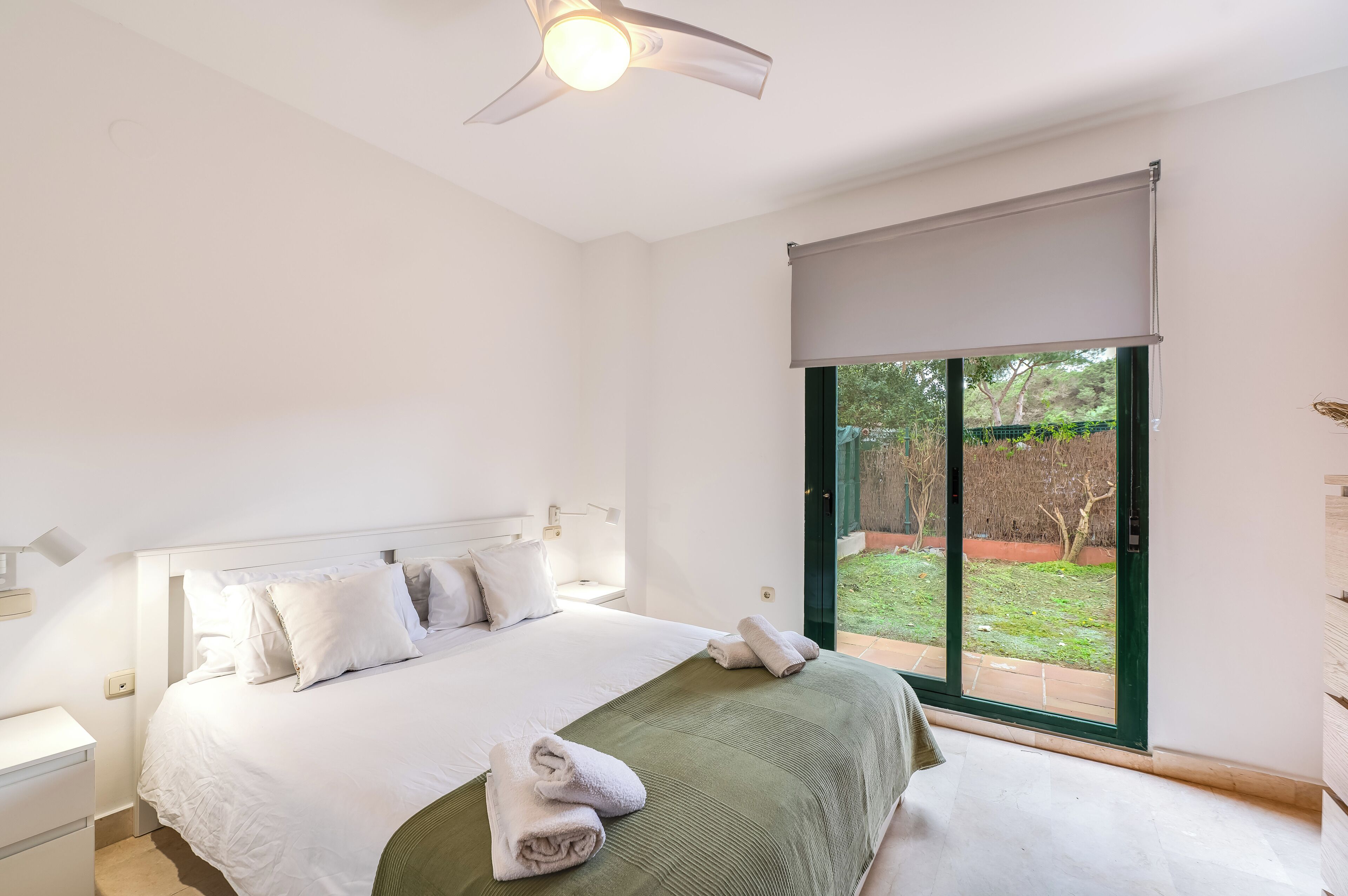 Een slaapkamer met een bed, een plafondventilator, een raam met uitzicht op de omgeving en een deur.