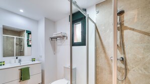 Un bany amb dutxa de vidre, un vàter, un lavabo amb mirall i una barra de tovalloles.