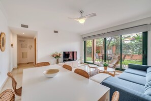 A modern living room with a dining area, a TV, and a large sliding glass door to an outdoor patio. - LXR Marbesa 1-Bedroom Near the Sea (Marbella)
