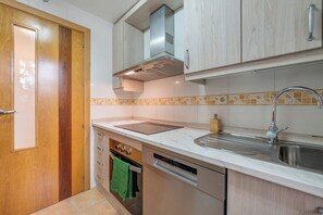 A modern kitchen with wooden cabinets, a stainless steel sink, a built-in oven, and a dishwasher. - LXR Marbesa 1-Bedroom Near the Sea (Marbella)