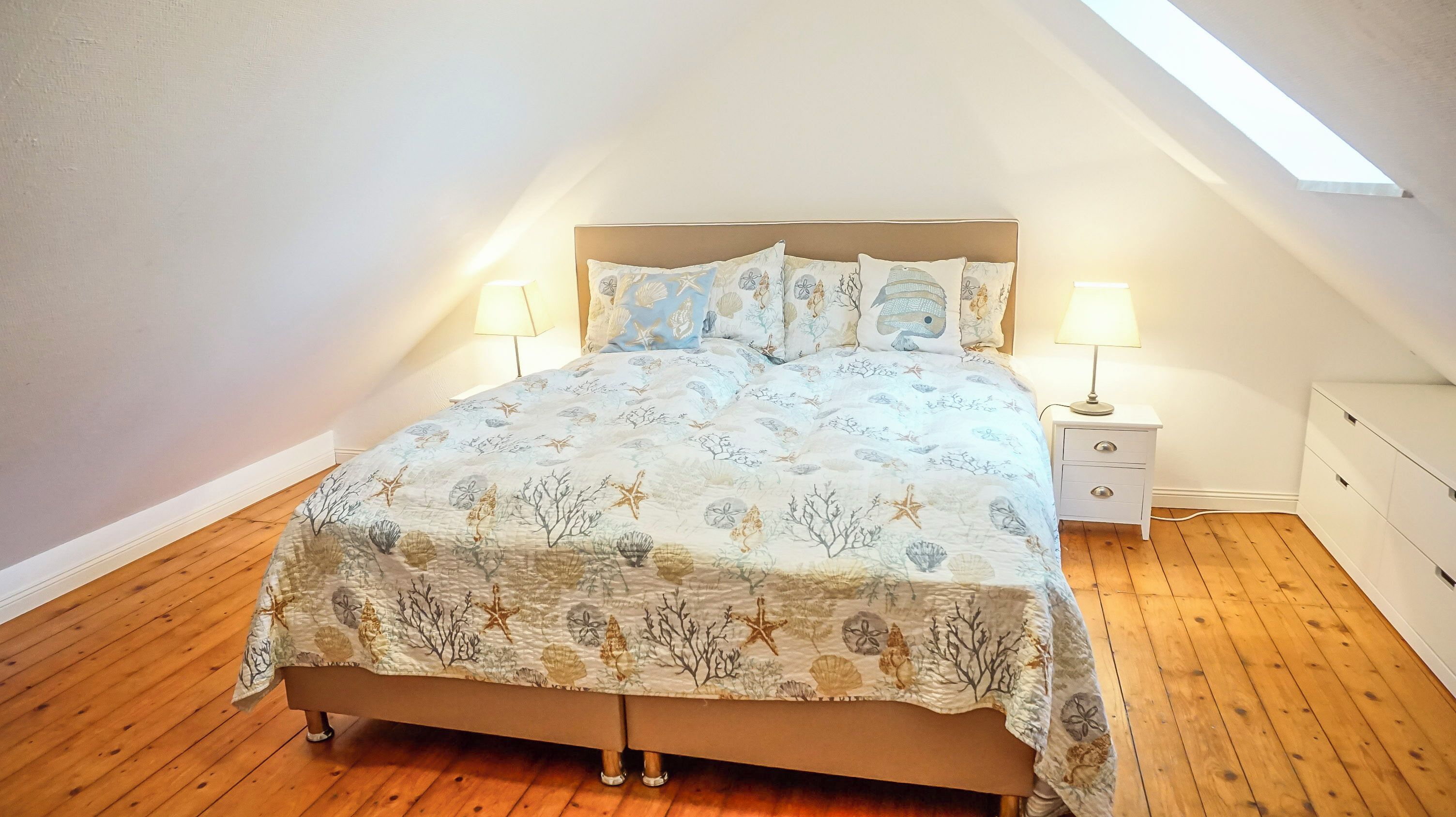 A bedroom with a bed, two bedside tables, a nightstand, and a skylight.