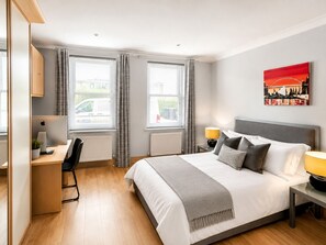 Ein Schlafzimmer mit Bett, Schreibtisch, Stuhl und Fenstern.