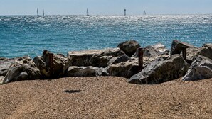 Un rivage rocheux, un ciel dégagé et des voiliers qui se dessinent à l’horizon.