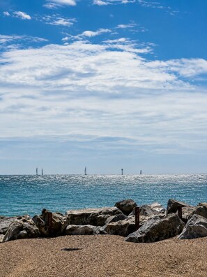 Eine felsige Küstenlinie mit blauem Himmel und fernen Segelbooten.