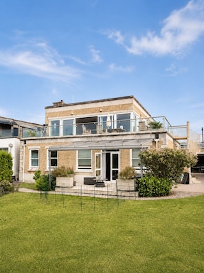 Ein zweistöckiges Haus mit Balkon, einem eingezäunten Garten und blauem Himmel.
