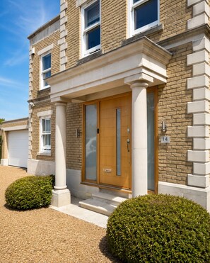 A two-story building with a brick facade, a wooden front door, and a garage door. - Fantastic Large Chichester Harbour View House. 2 minutes to beach. (Hayling Island)