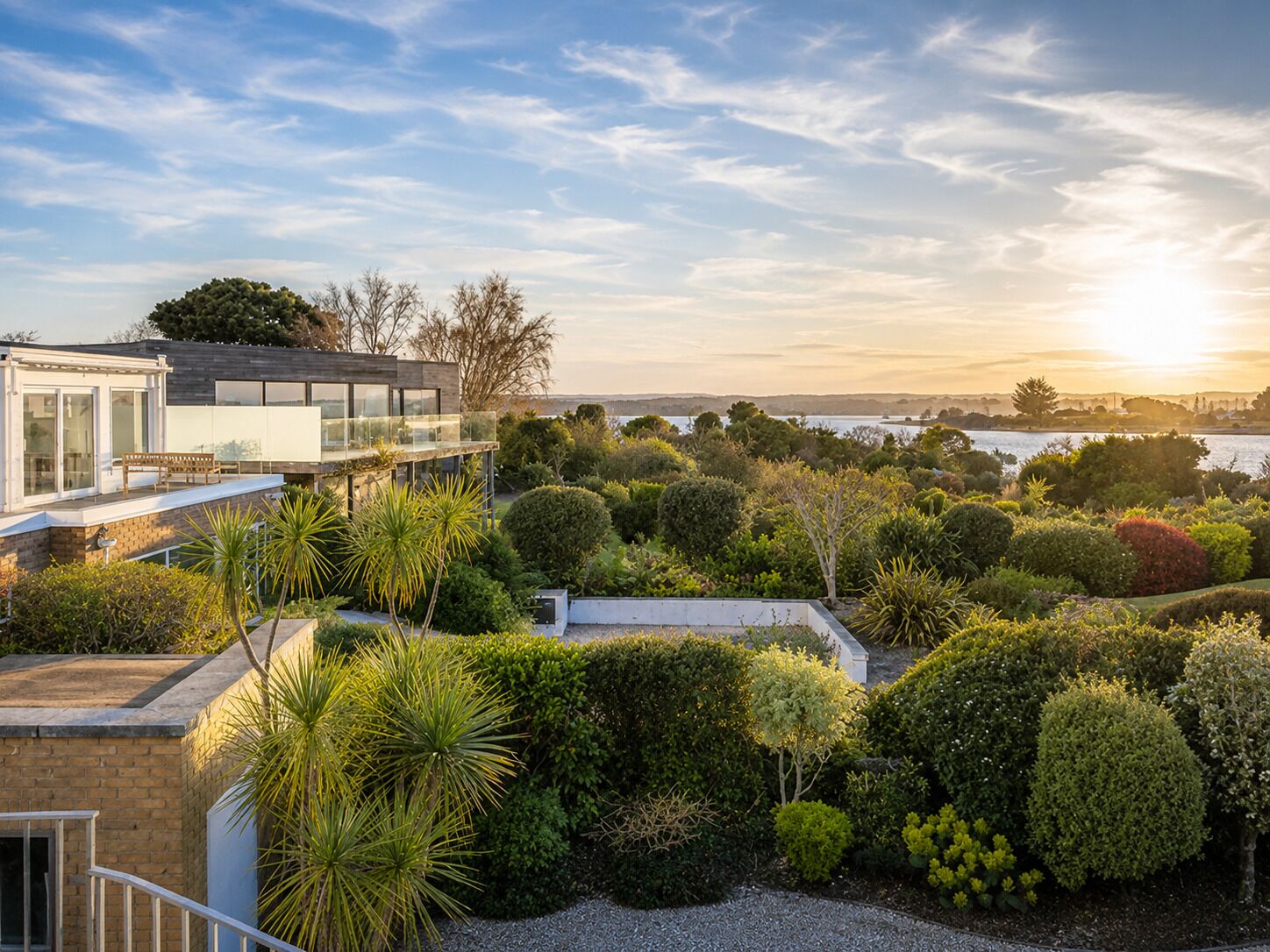 Une maison moderne dotée d’un balcon donnant sur un jardin aménagé et offrant une vue sur l’eau.