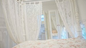 Un dormitorio con cama con dosel, un baño a la vista con lavamanos y un armario con espejo.