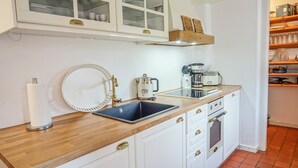 Una cocina con un lavamanos, una cafetera y un armario con puertas de vidrio.