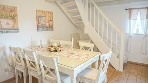 Un comedor con mesa de vidrio, sillas blancas, una escalera y obras de arte en las paredes.