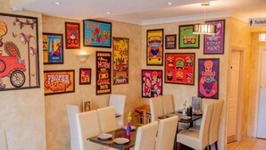 A dining area with tables and chairs, a wall with colorful posters, and a sign indicating the location of the toilet. - Standard Twin Room (Norwich)