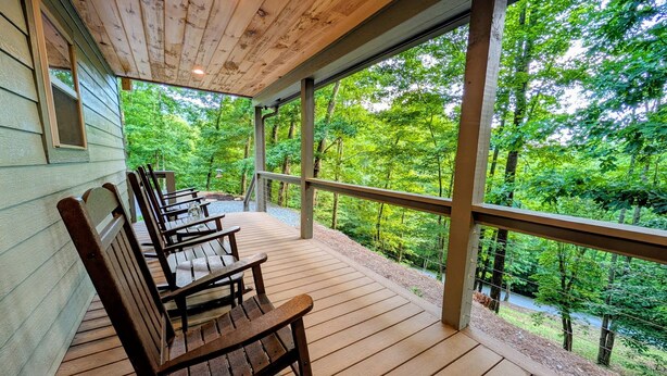 A wooden deck with benches, large windows, and a view of a forest. - Mountain Breeze (Bryson City)